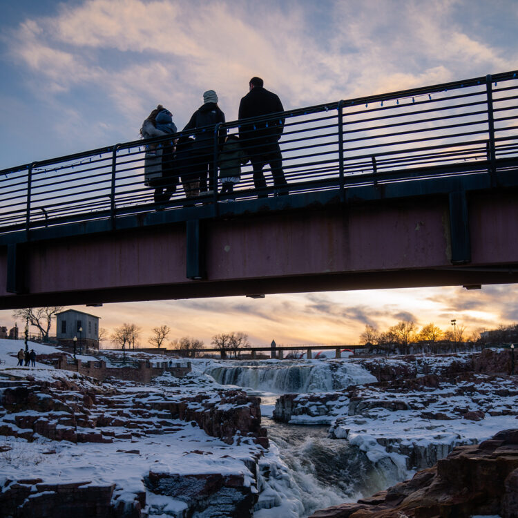 A family gathers on the bridge at falls park enjoying the beautiful sight of the falls covered in snow